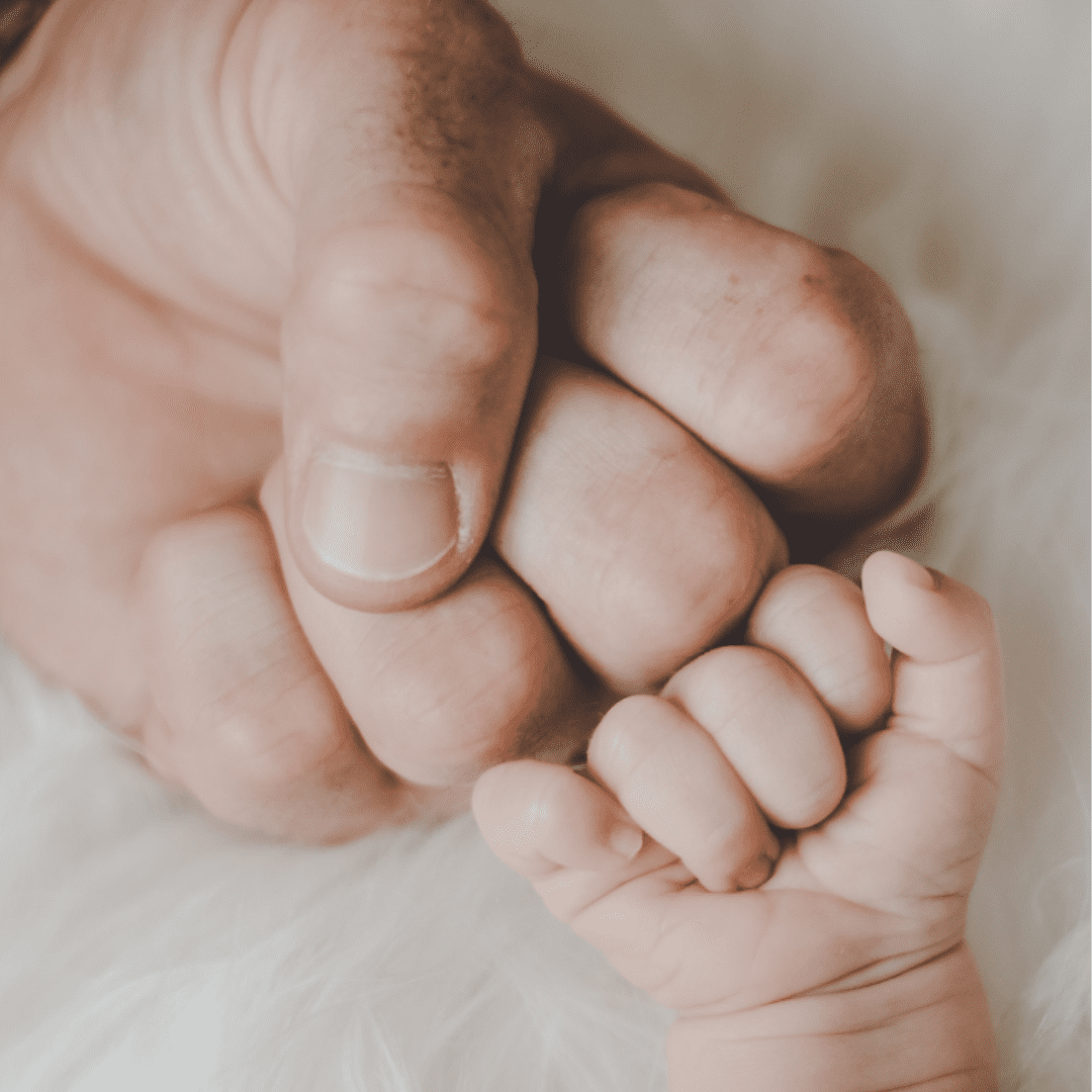 An adult hand holding a baby's hand